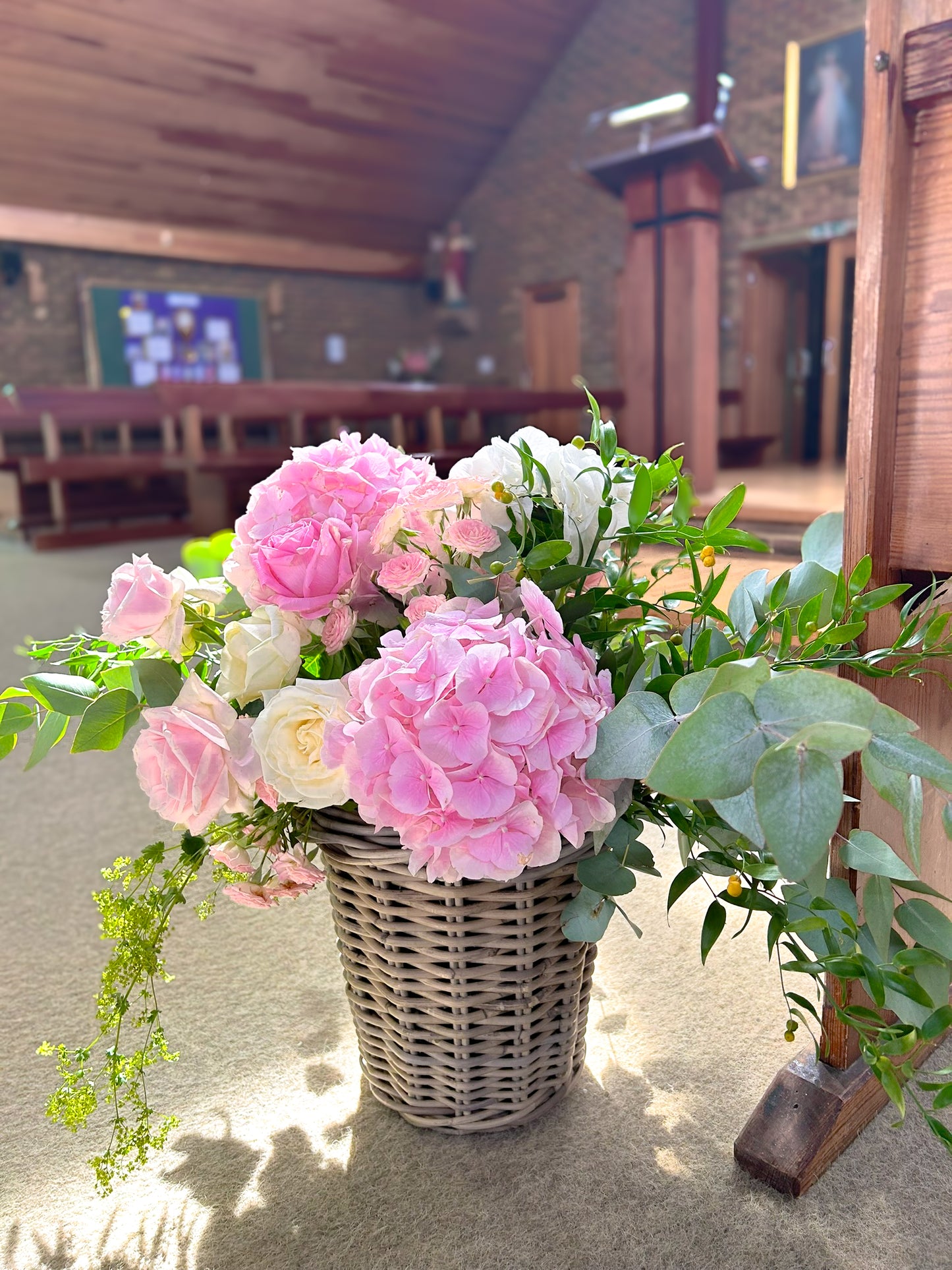 Bouquet of pink and white flowers in a woven basket on the floor.