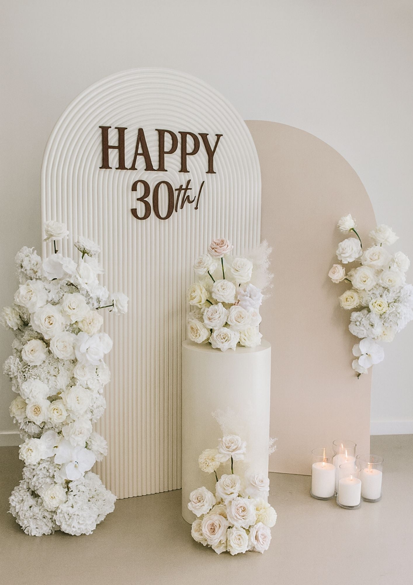 Decorative arch with 'Happy 30th!' sign, surrounded by white flowers and candles.