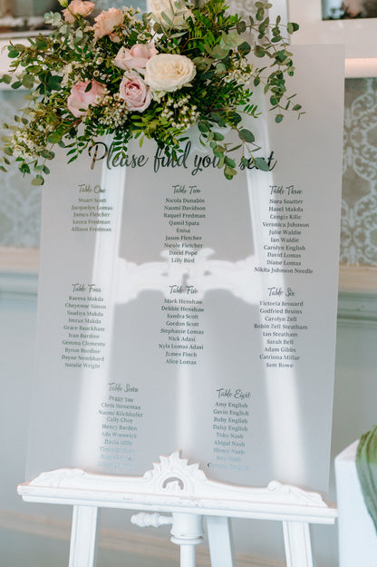 Seating chart with floral arrangement on a white stand
