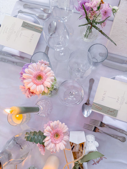 Elegant table setting with flowers, glasses, and cutlery on a white tablecloth.