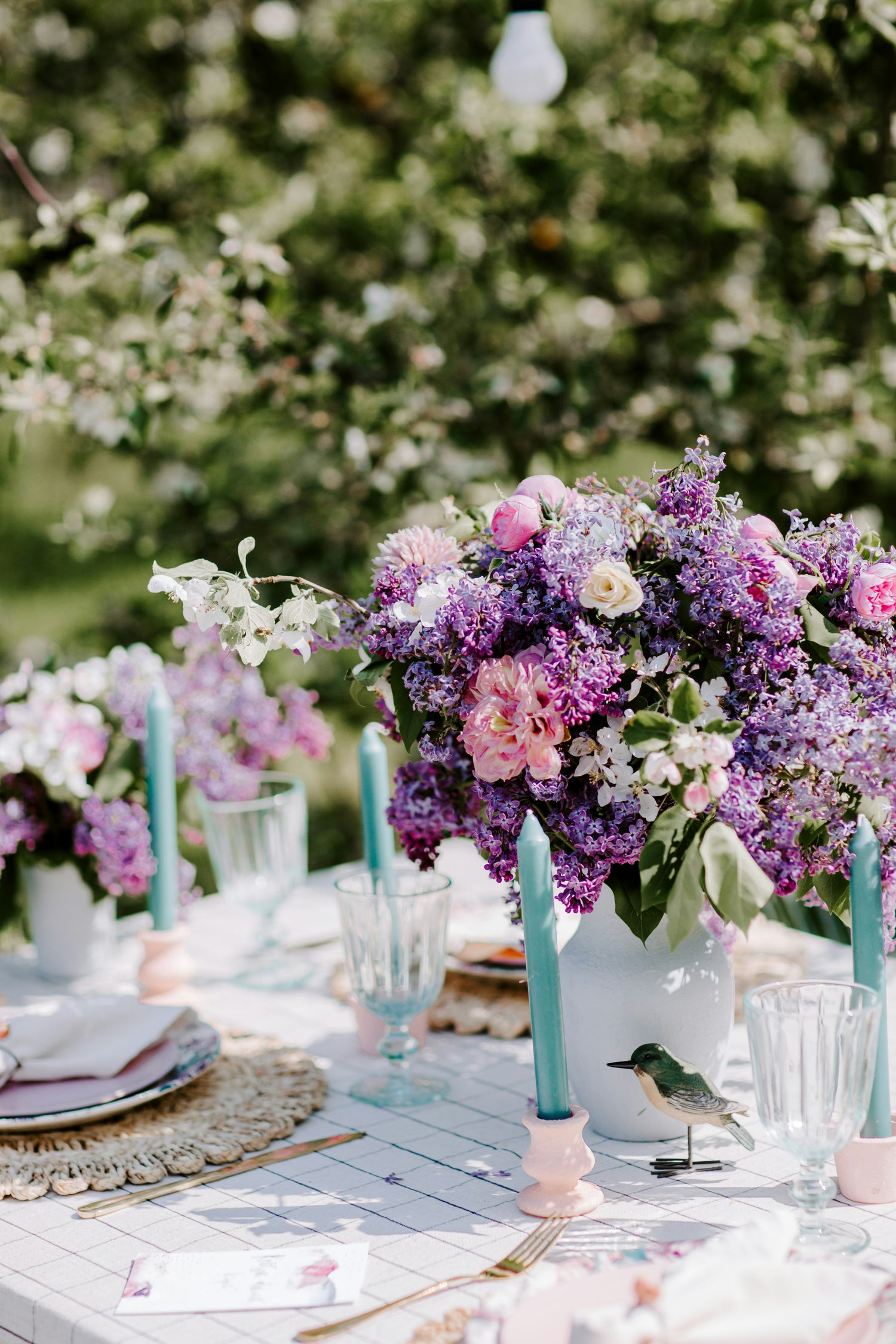 Decorative table setting with pink and purple flowers and candles in an outdoor setting
