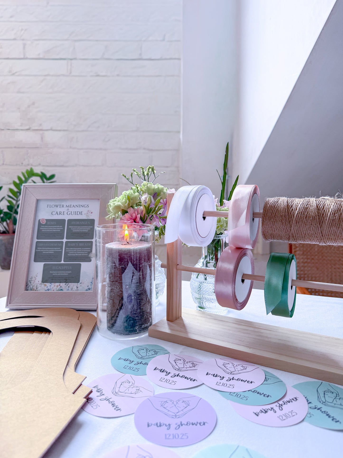 Decorative setup with spools of ribbon, a lit candle, and printed cards on a table.