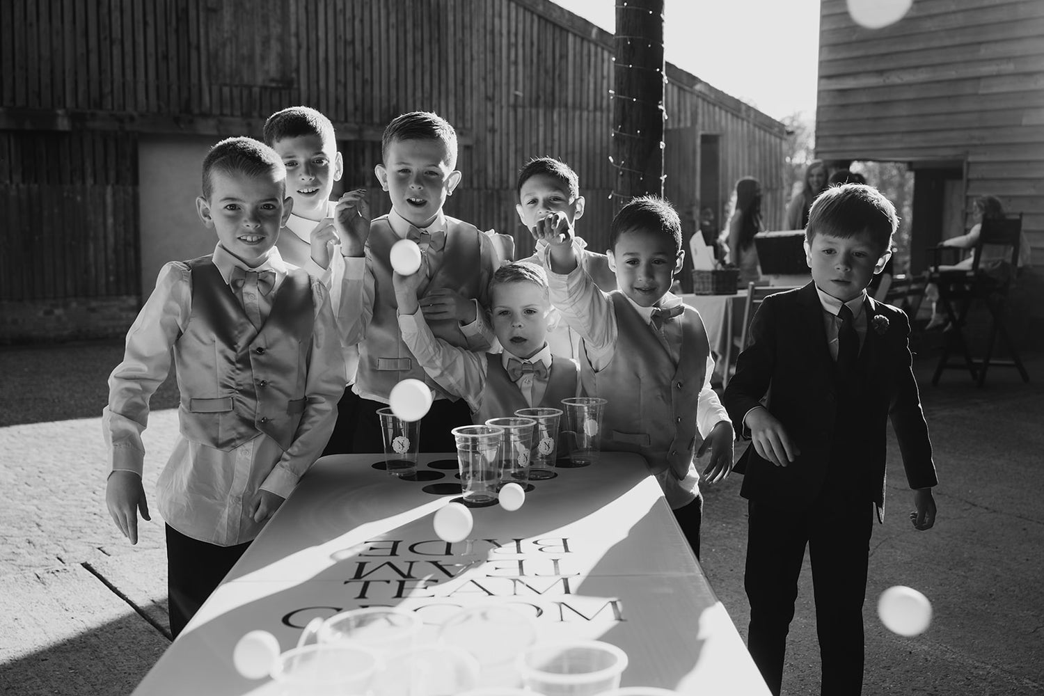 Group of boys in formal attire standing around a table with drinks, outdoors.