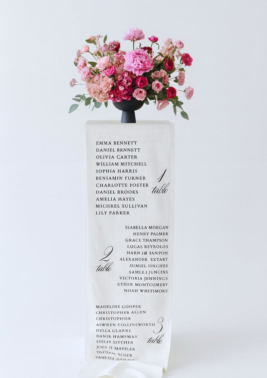 Premium fabric table seating chart with floral arrangement on pedestal.