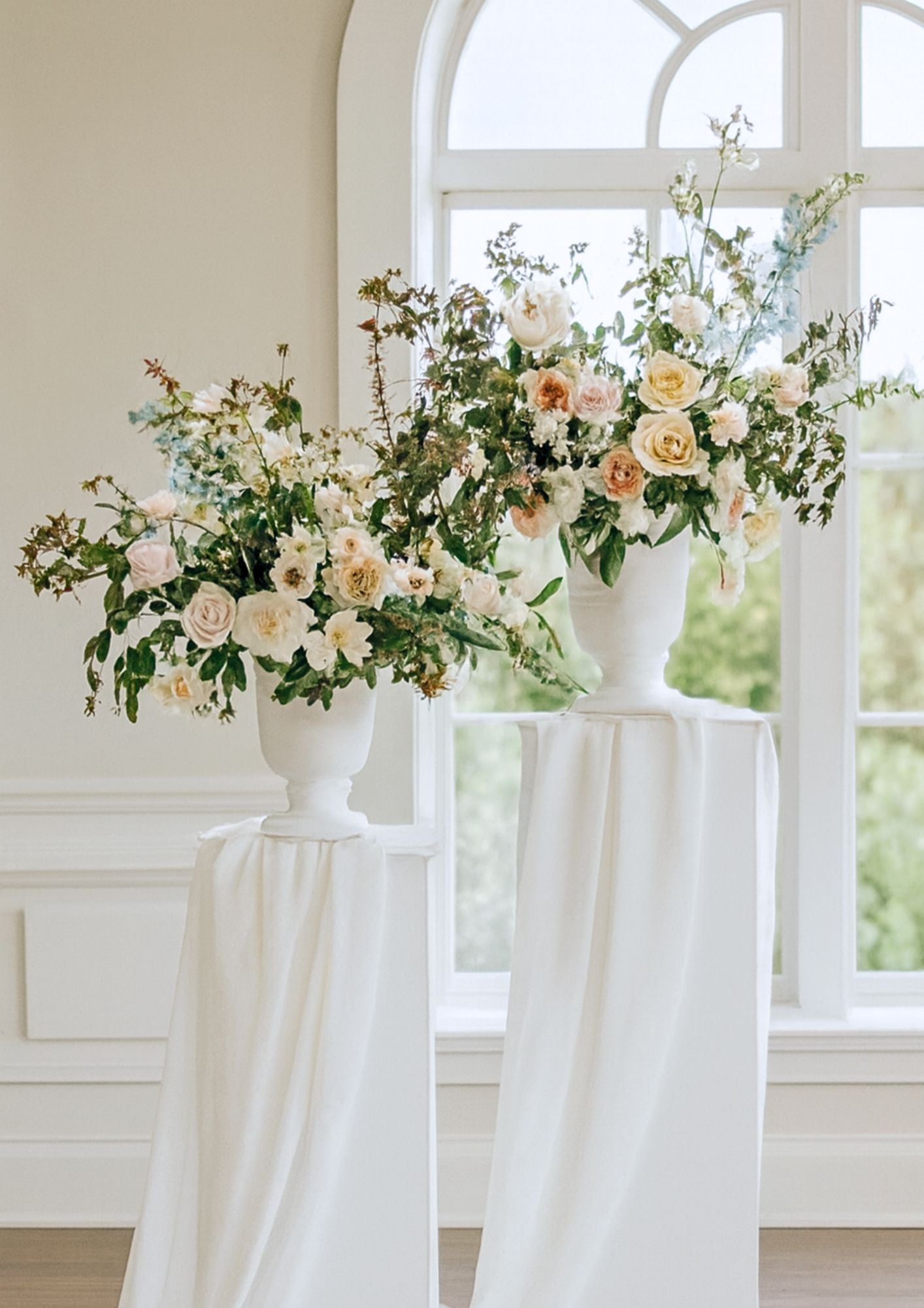 Floral arrangements in white vases on a pedesteral on a white tablecloth