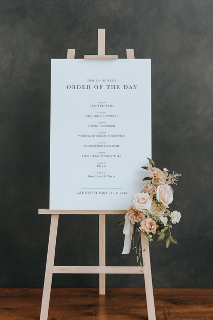 Order of the Day sign on an easel with floral decorations.