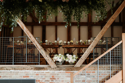 Decorated  wedding indoor setting with wooden beams, tables, and floral arrangements.